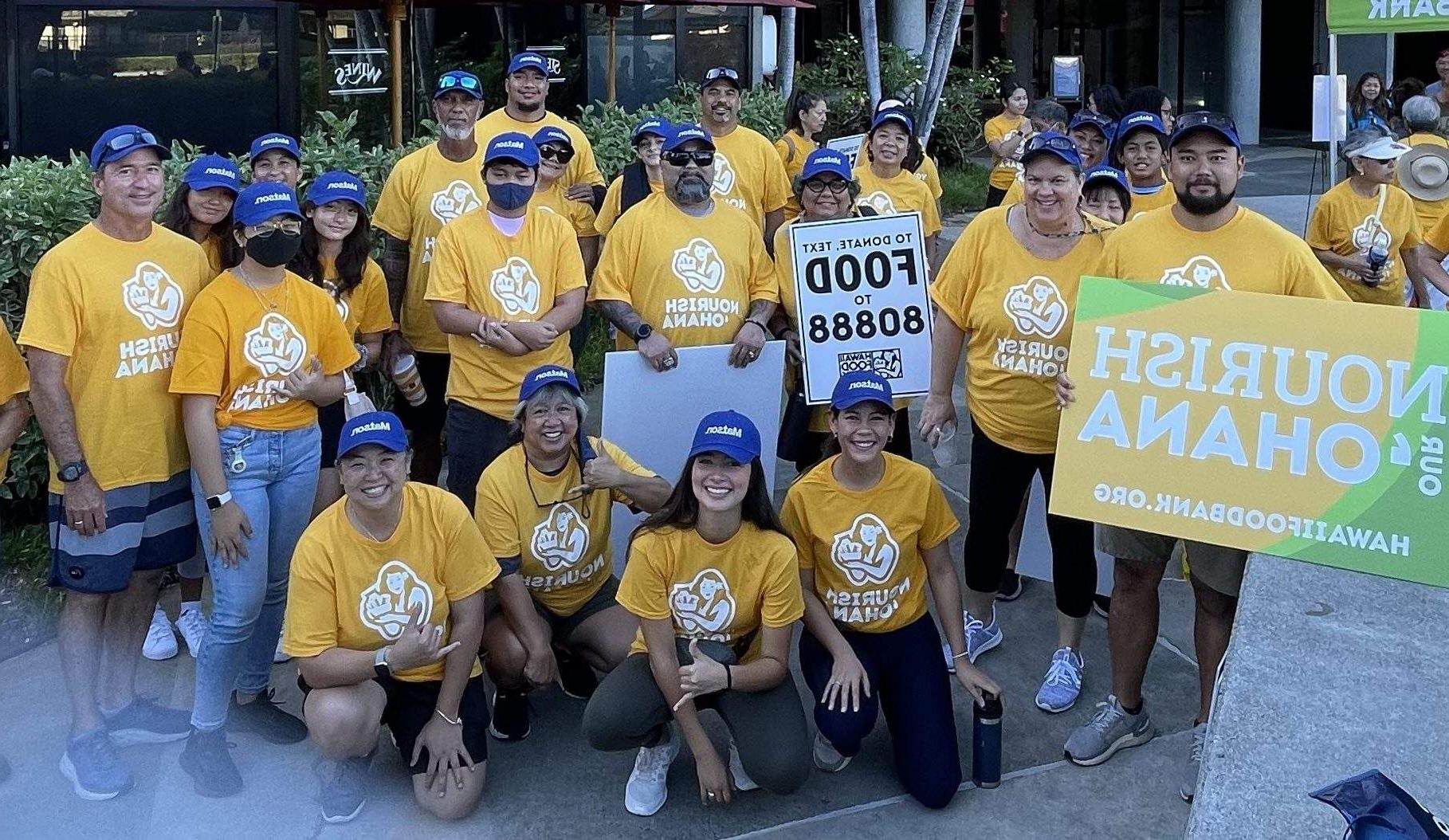 澳博体育app下载 volunteers wearing blue 澳博体育app下载 hats and yellow Nourish Ohana t-shirts pose for a group picture.